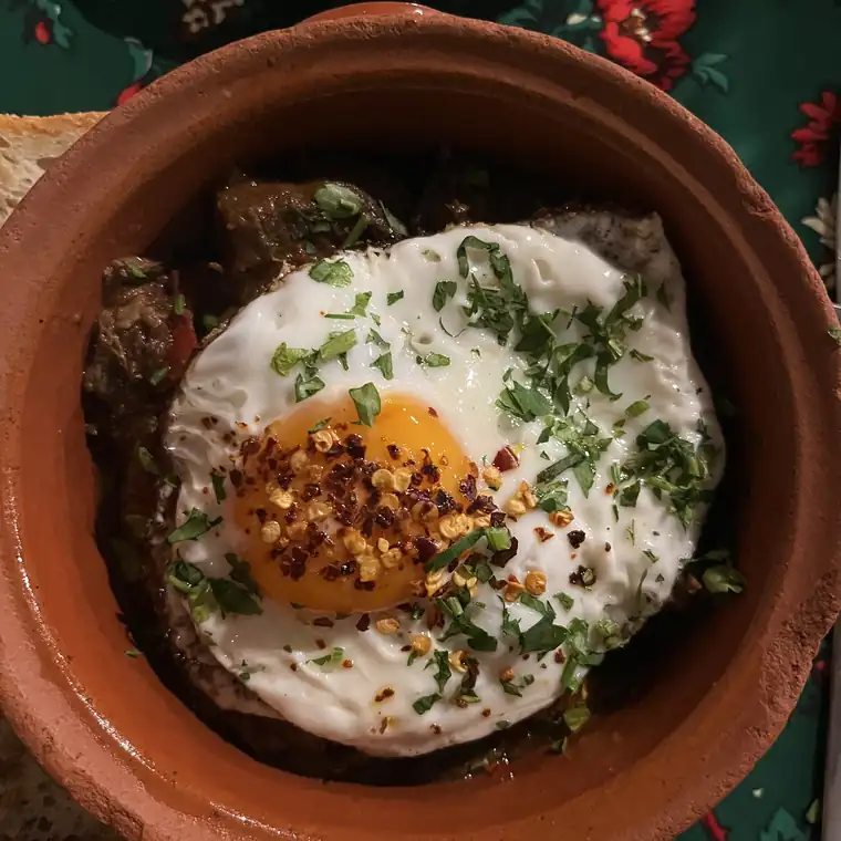 Gjuwecz w glinianym garnku z jajkiem sadzonym, płatkami chili i natką